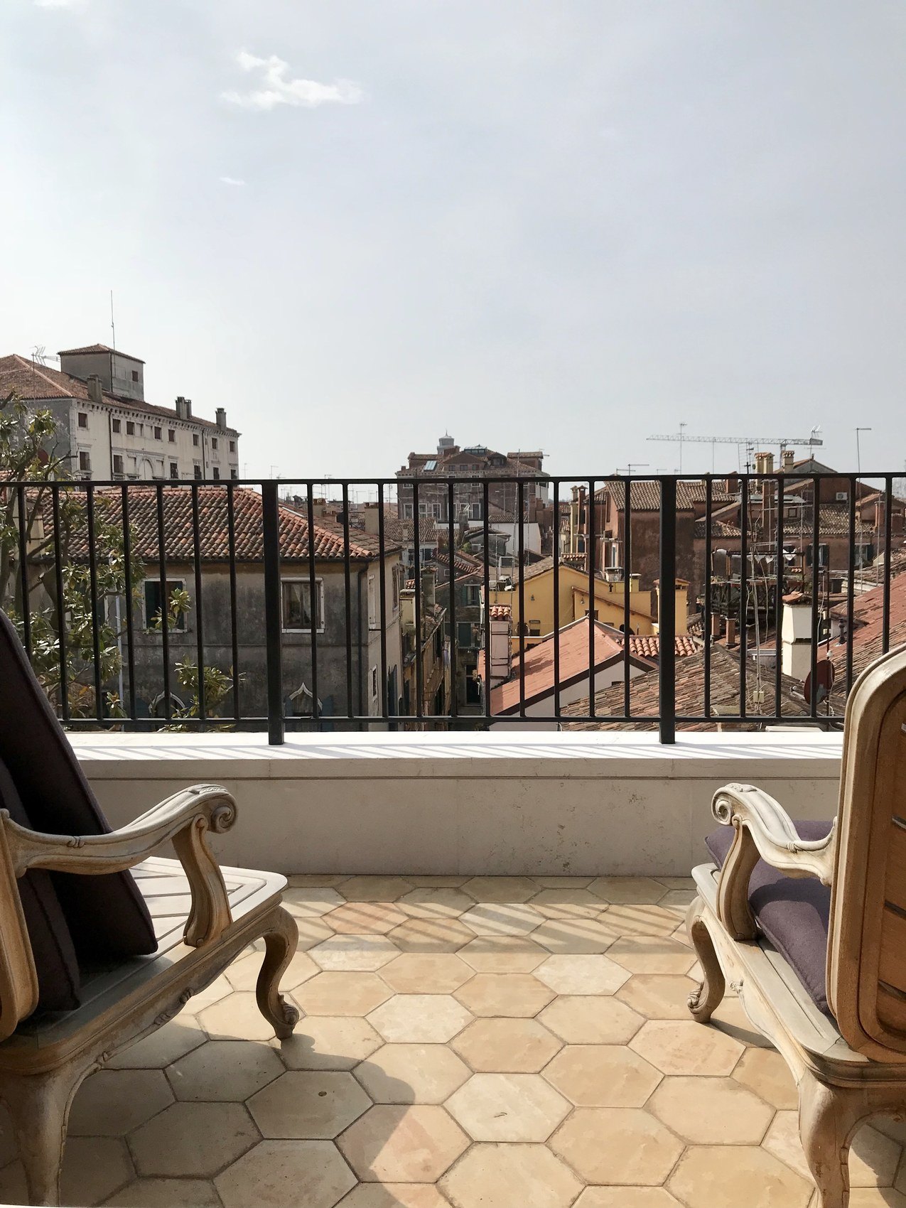Two painted armchairs on a hexagonal tiled roof terrace over the rooftops of the city