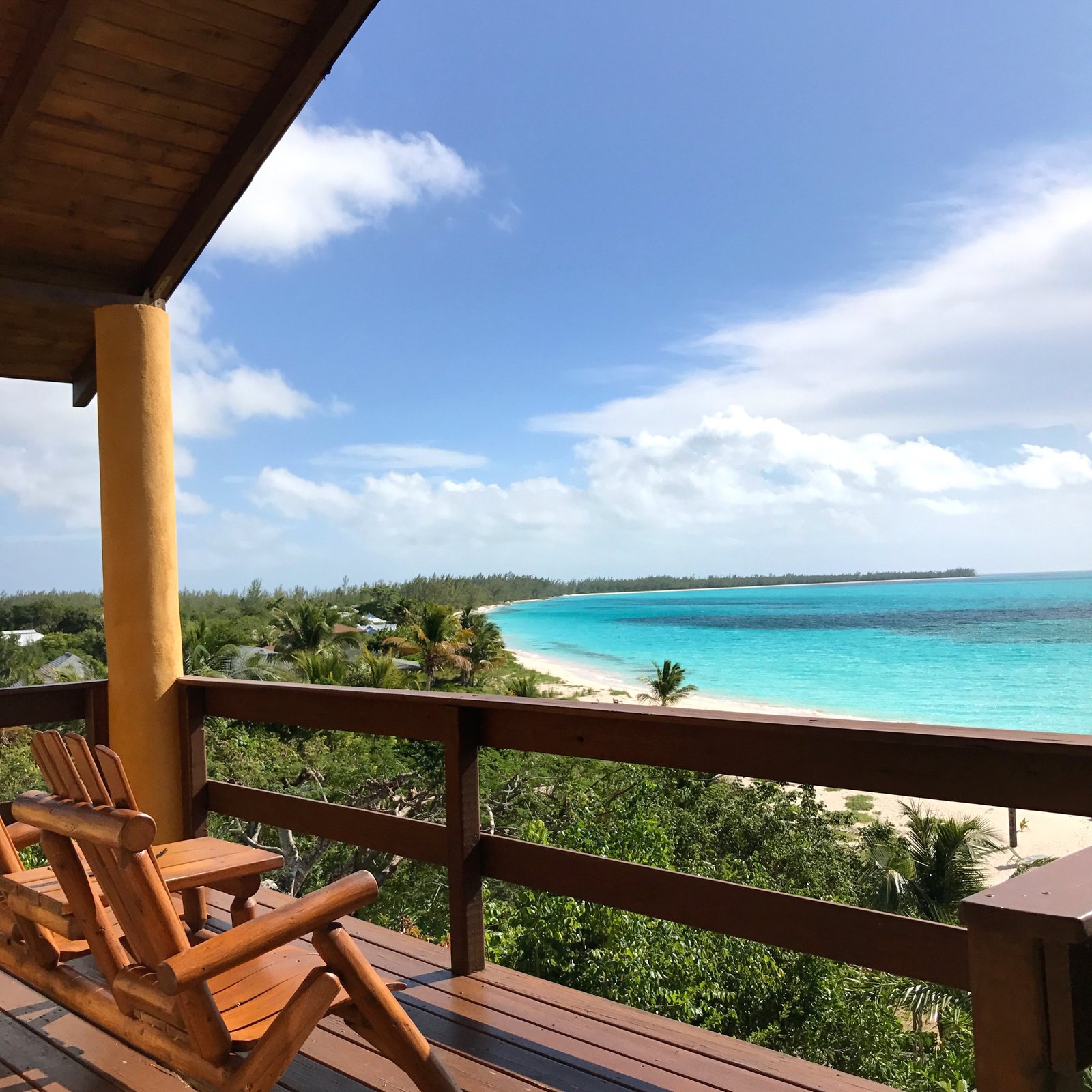 Two log armchairs on a timber veranda looking along a turquoise bay to the far point