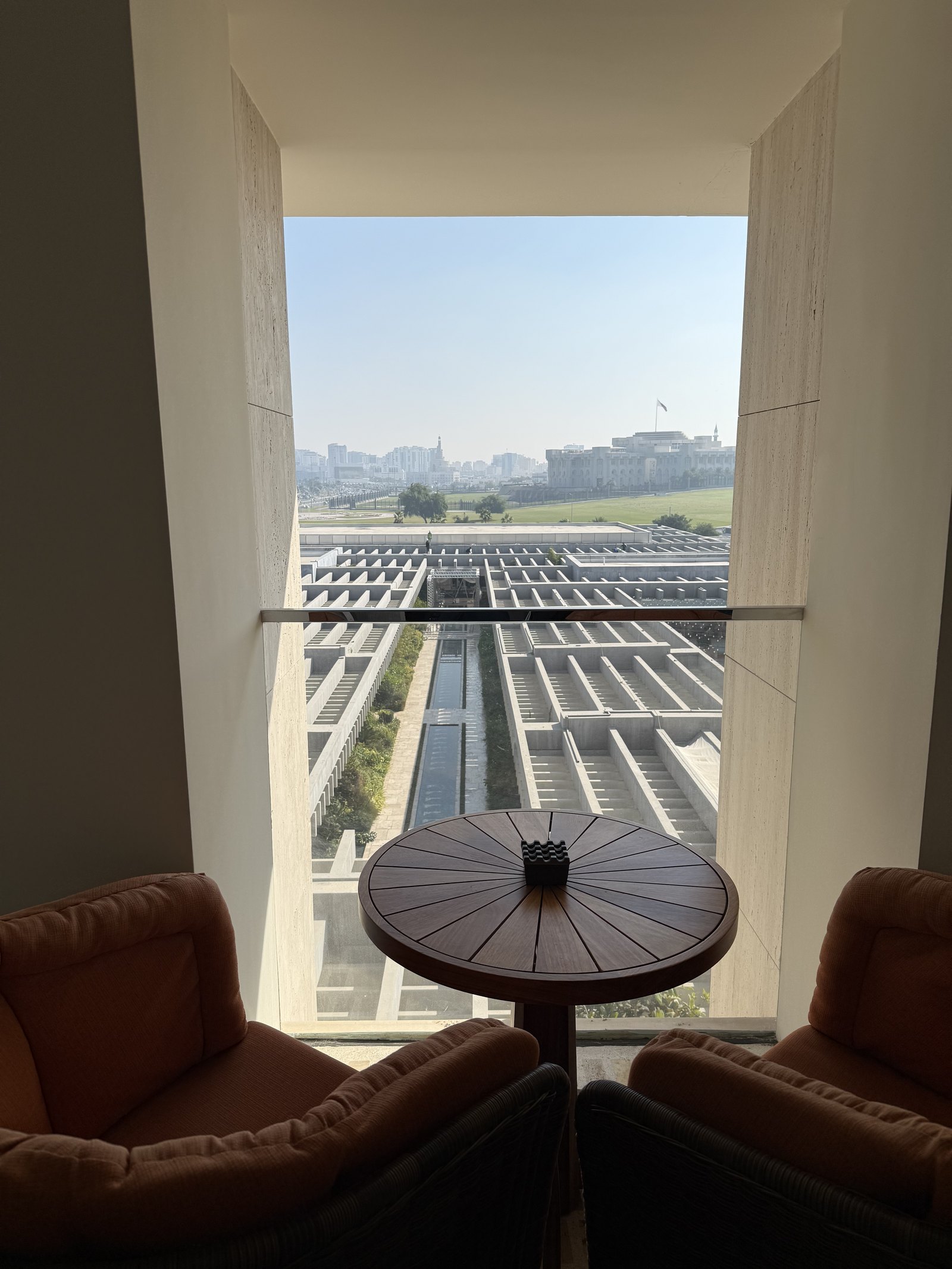 A small round table and two leather armchairs in a deep window, looking out over a ribbed roof to the skyline