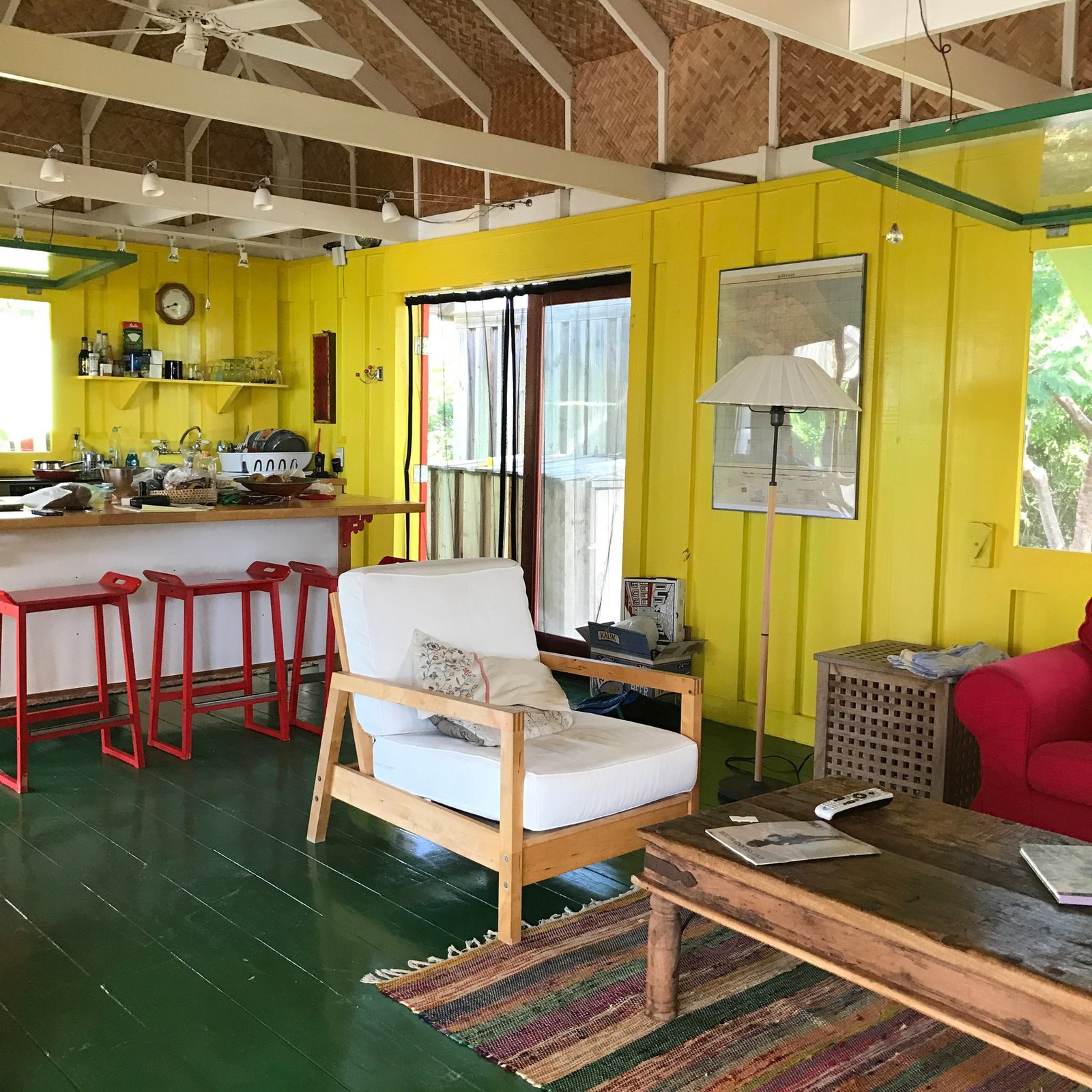 A yellow timber room with a kitchen counter and red stools, green painted floor